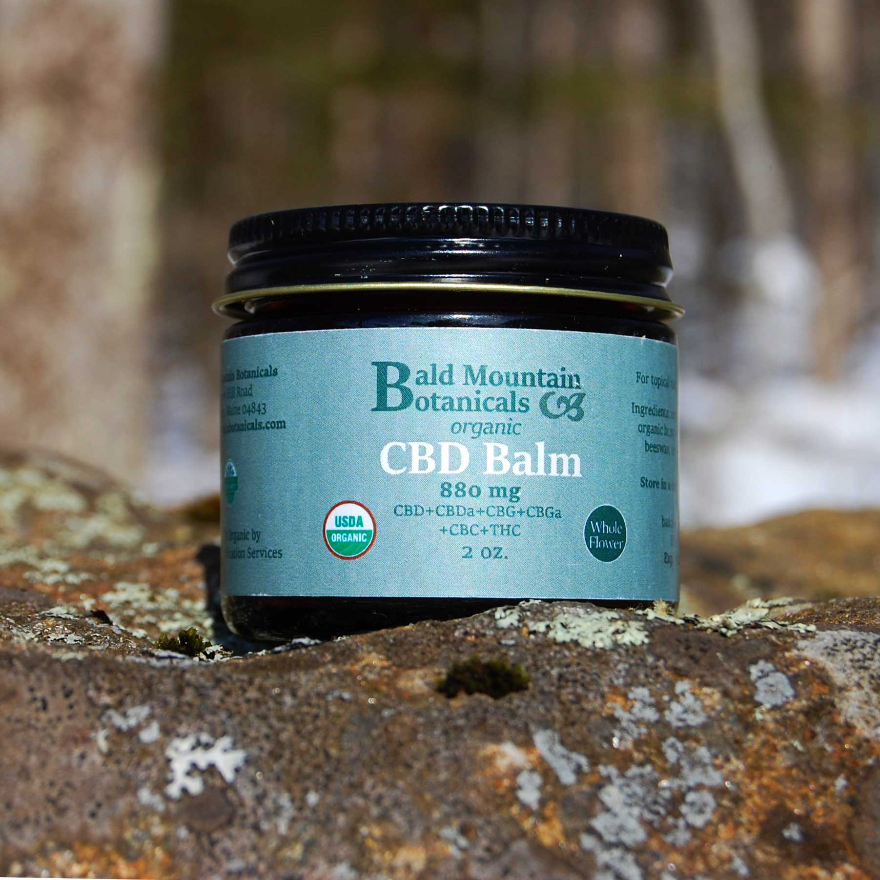 glass jar of whole-flower CBD Balm on stone with woods in background