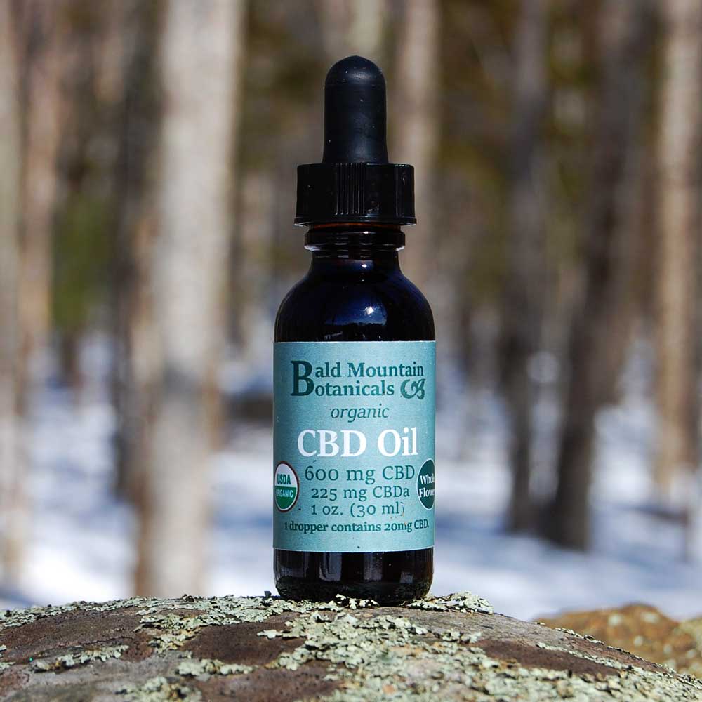 brown glass eyedropper bottle of organic whole flower CBD oil on stone with winter woods in background